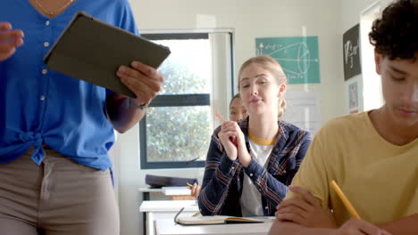 in high school, teenage girl raising hand while teacher using tablet in classroom