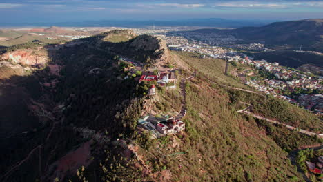 자카테카스의 세로 데 라 부파 (cerro de la bufa) 의 드론 영상으로 산과 그 상징적인 케이블카 지역을 둘러싼 웅장한 반 도를 보여줍니다.