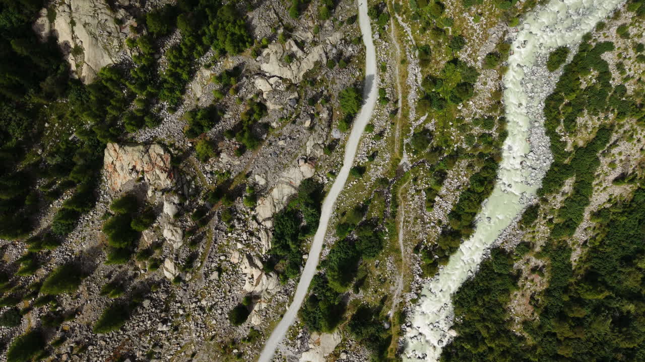 Drone shot in full top-down view following a winding trail through Morteratsch Valley between the mountains in Switzerland