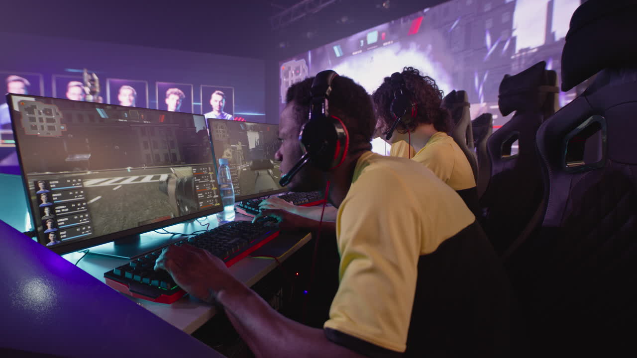 young Cyber Sportsmen during Gaming Tournament Multiracial Young Esportsman Gamers Playing Shooter on Computers Near Large Monitor with Match Broadcast during Professional Gaming Competition Battle