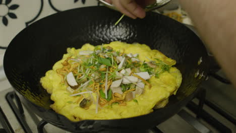 adding shredded greens into big asian frying pan with egg and abalone