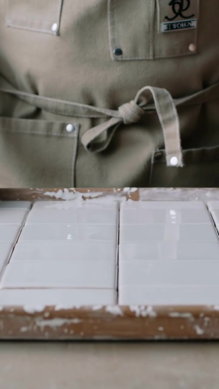 Vertical video: Recording person wearing green apron behind tile frame on table watching grout dry