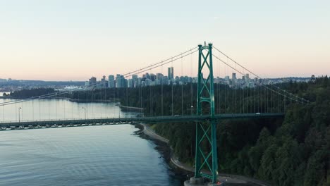 Toma-Aérea-De-Un-Dron-Volando-Lejos-Del-Puente-De-La-Puerta-De-Los-Leones-De-Vancouver-Con-El-Paisaje-Urbano-En-El-Fondo