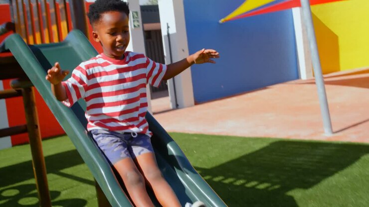 Vista frontale di scolaro afroamericano che gioca sugli scivoli nel parco giochi della scuola 4k