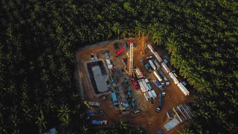 cinematic 4k drone footage of onshore drilling rig equipment structure for oil exploration and exploitation in the middle of jungle surrounded by palm oil trees during sunset and high oil price