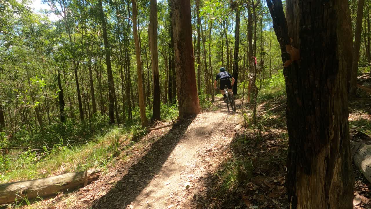 ciclista de montaña de campo traviesa pasando rápidamente la cámara en un sendero australiano seco con un pequeño látigo sobre una joroba