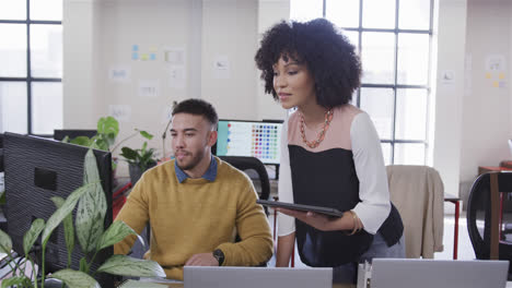 Portrait-of-happy-diverse-male-and-female-colleague-at-desk-using-tablet-and-computer,-slow-motion