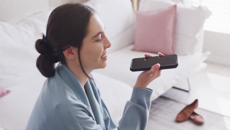 happy caucasian woman sitting on couch and talking on smartphone