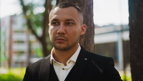 man in classic black suit looks aside standing in city park