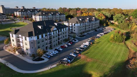 parking cars in front of noble apartment houses during golden sunset. autumnal day in suburbia of american town. walking elderly person with dog. retirement apartments in america. descend aerial view.