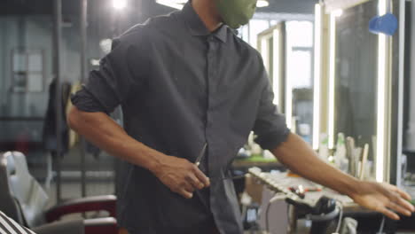 Barber-in-Protective-Mask-Spraying-Water-on-Hair-of-Man