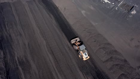 aerial tracking shot of digger working on coal mining field and transporting coal
