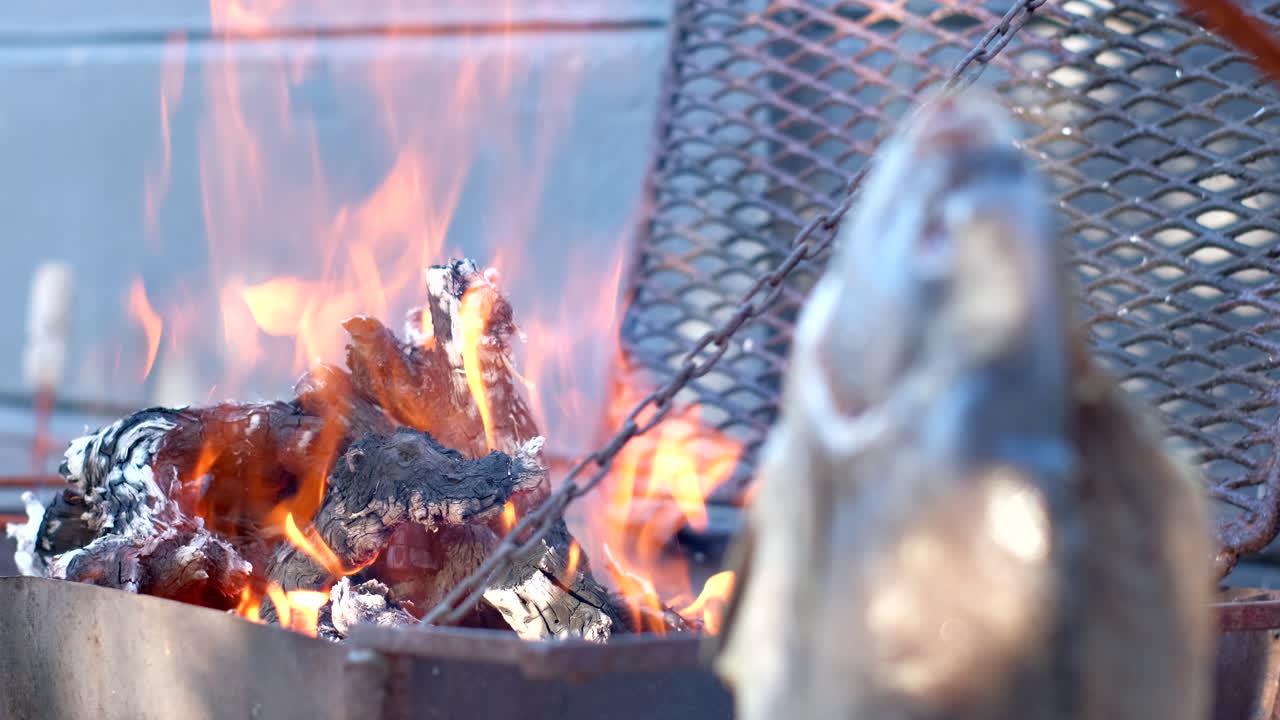 Fuoco di legna ardente con pesce appeso che si asciuga a goccia per un barbecue all'aperto.