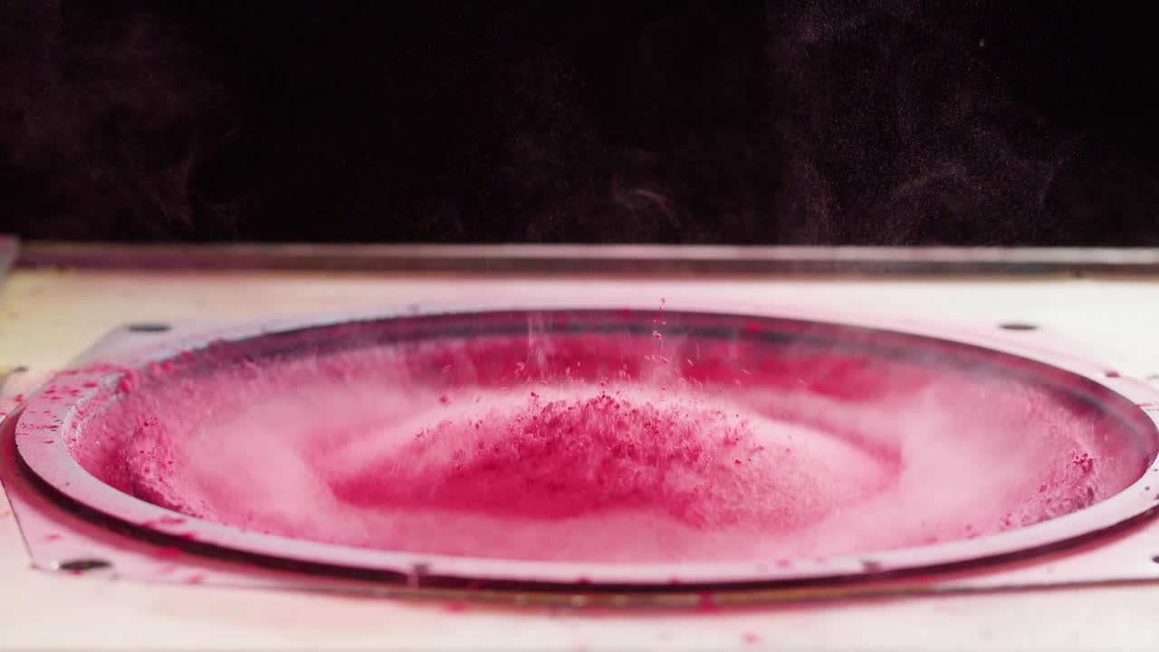 Levende pink pulver danser på en højttalermembran i slowmotion.