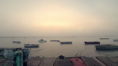 El-Tranquilo-Resto-De-Pequeños-Barcos-Pesqueros-Sobre-El-Agua,-Abrazados-Por-La-Niebla-Y-La-Niebla,-Mientras-Los-Rayos-Del-Sol-Crepusculares-Otorgan-Un-Resplandor-Tranquilo,-Elevando-La-Esencia-De-La-Vida-Marina.