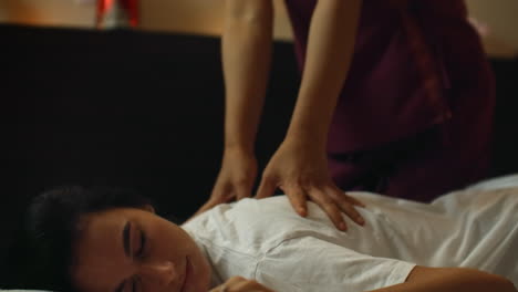 alternative chinese medicine an asian woman performs therapeutic massage on the back and legs of a caucasian woman lying on a couch. aromatherapy and manual therapy by chinese masters.