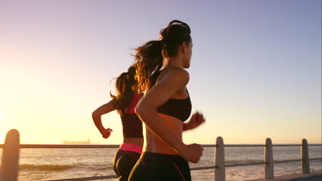 two women running along the beach at sunset