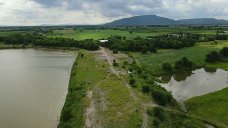 Aerial-ascending-footage-of-such-a-gorgeous-farm-and-provincial-landscape,-lake-on-the-left,-pond-on-the-right,-dirt-roads-around,-Muak-Klek,-Saraburi,-Thailand