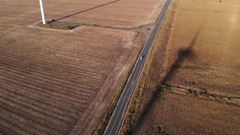 Auto-Fährt-Auf-Einer-Landstraße,-Vorbei-An-Windkraftanlagen-Bei-Sonnenuntergang