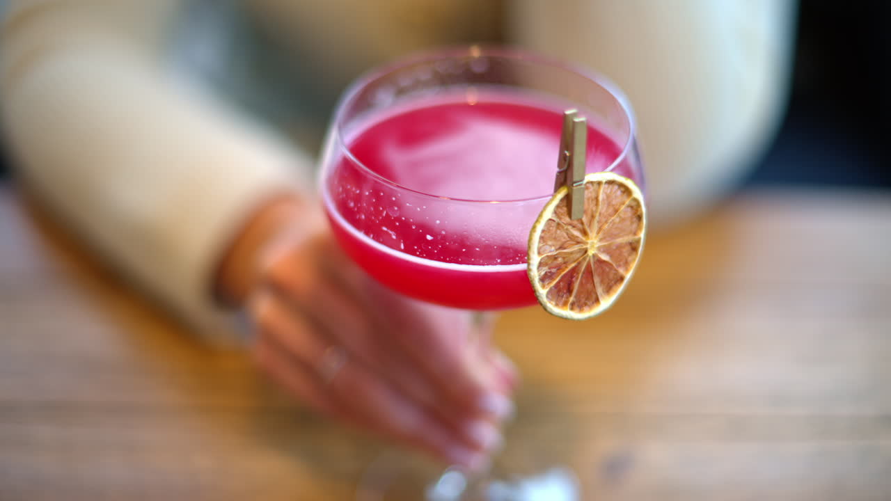 Kvinde drikker rød cocktail med tørret appelsin som pynt