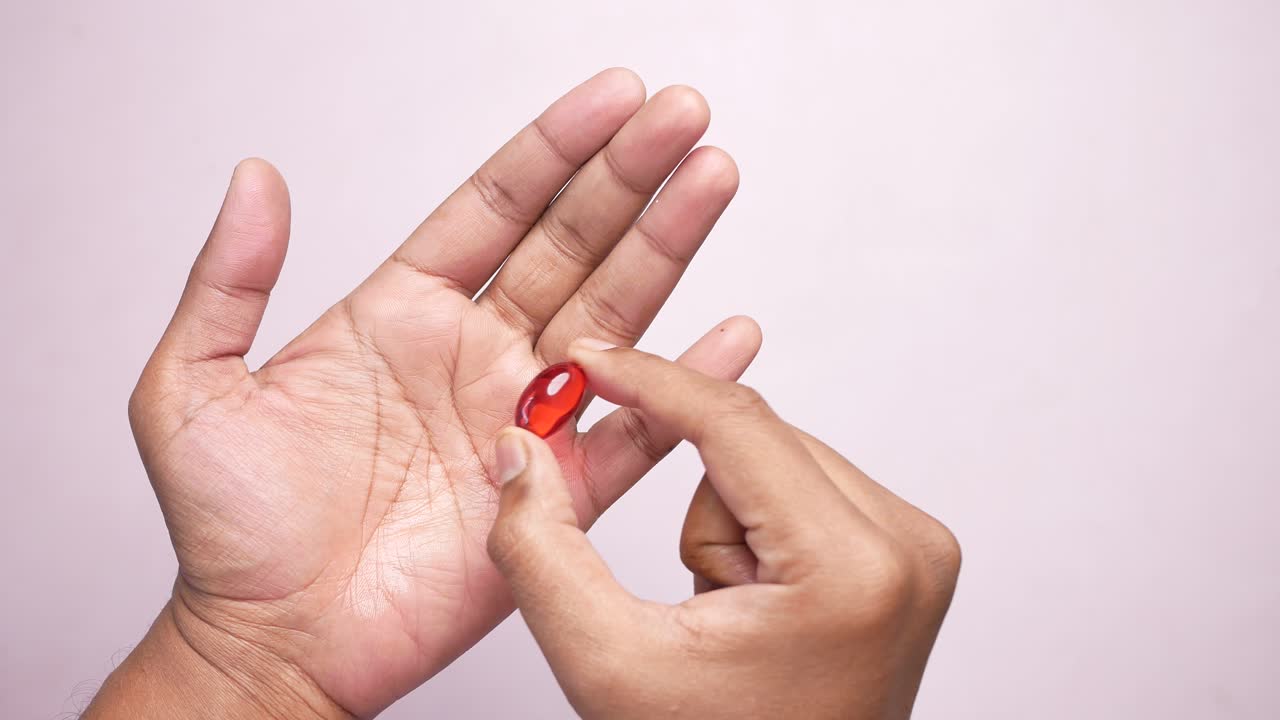 primer plano de una persona sosteniendo una pastilla de cápsula roja