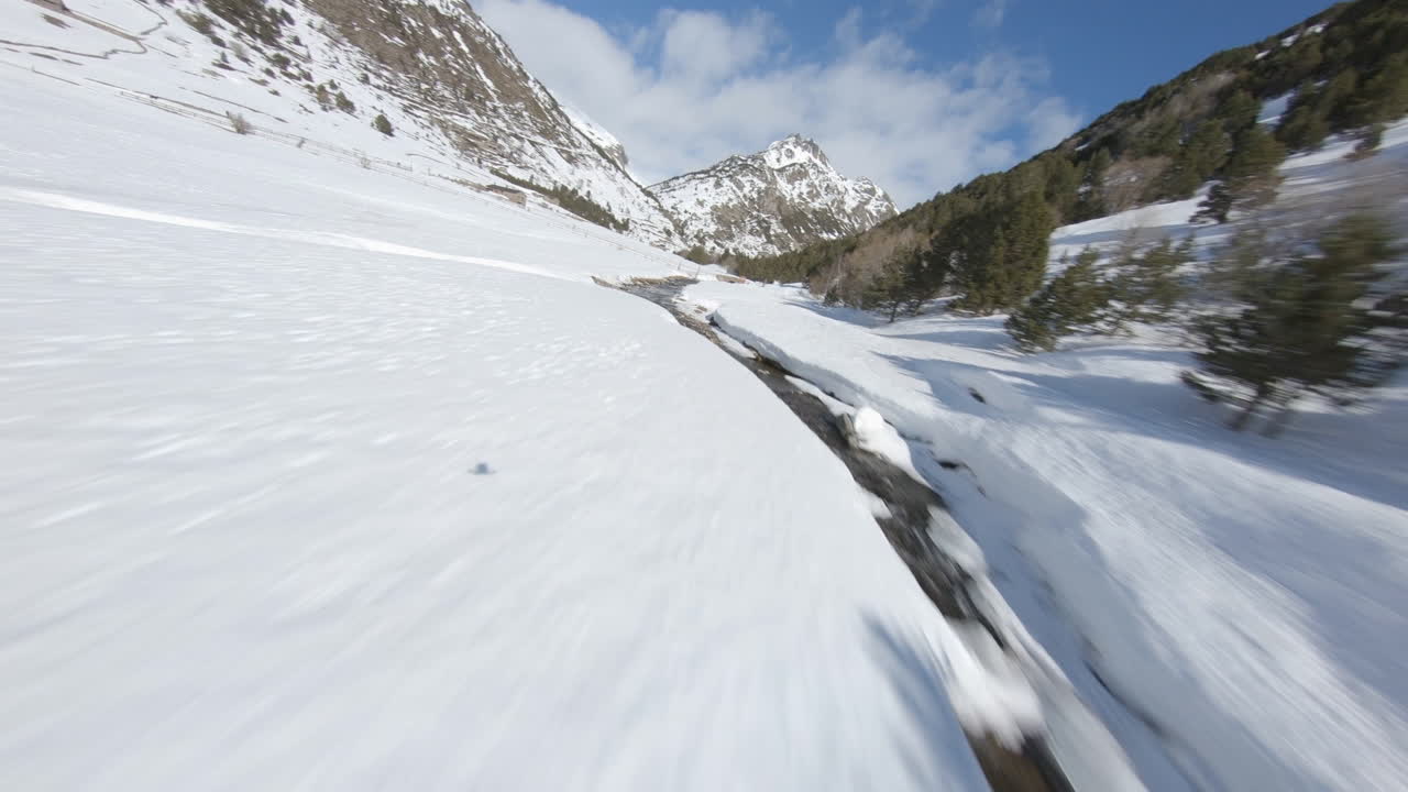 Aerial drone fpv over stream flowing in snowy and frozen Incles valley, Pyrenees