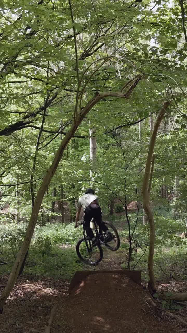 Drone Vertical Video Tracking Man On Mountain Bike Cycling Doing Mid-Air Jump On Trail Through Woodland 2