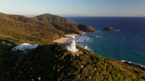 wide cinematic drone shot rotating around smoky cape lighthouse in australia revealing green island, the ledge and the pacific ocean