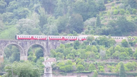 wide view of a red train over a historic bridge in the douro river valley, portugal in summer