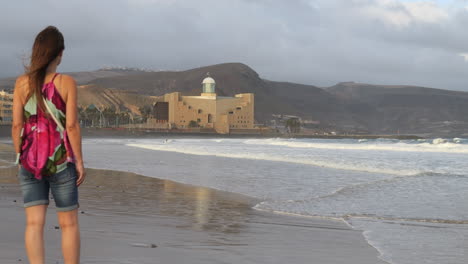 Plano-Cinematográfico-De-Una-Mujer-Admirando-El-Auditorio-Alfredo-Kraus-Mientras-Las-Olas-Rompen-En-La-Orilla-De-La-Playa-De-Las-Canteras,-En-La-Isla-De-Gran-Canaria