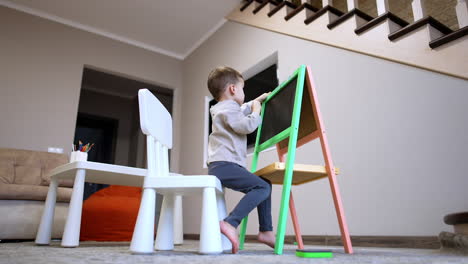 young child drawing at a colorful easel. a child engages in drawing on a green and pink easel while sitting on a chair in a cozy living room