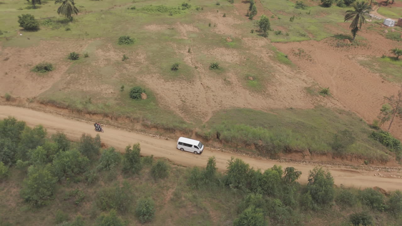 Turning drone shot of a white bus or van driving on a rocky road near the rural town of Kimina Bujumbura Burundi Africa on a warm day LOG