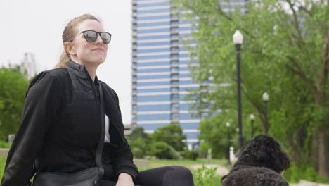 young woman sitting on a park bench in a city with her dog next to her