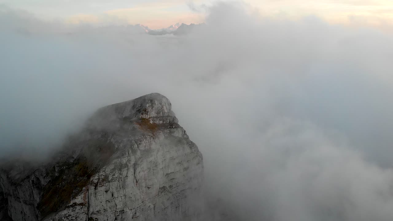 Aerial flyover through clouds in Leysin, Vaud, Switzerland during an autumn sunset with Dents du Midi and Tour de Mayen in the view and with hikers on Tour d'A&iuml; waiting for clouds to disappear