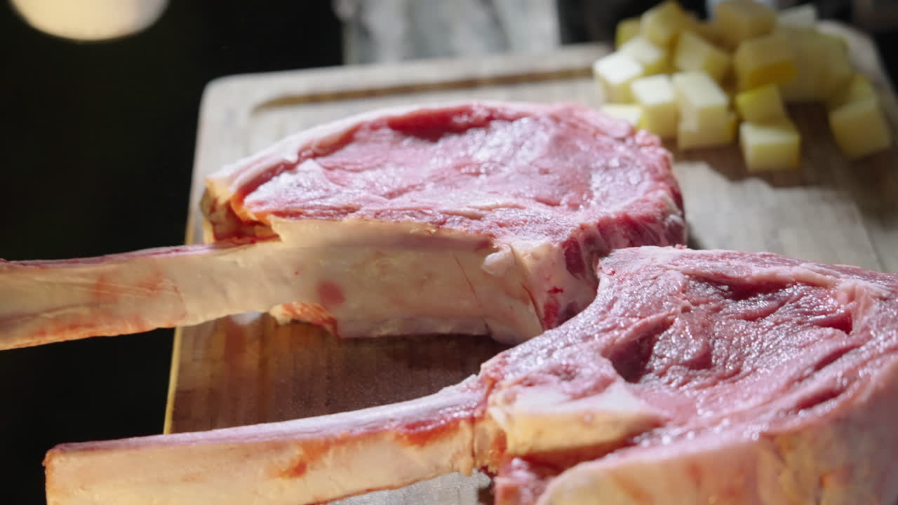 Hand Seasoning Raw Tomahawk Steaks on a Cutting Board