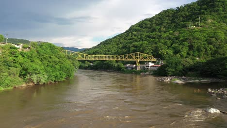 Aerial-view-of-a-bridge-above-muddy-Magdalena-river-and-green-hills-of-colombian-highlands-near-Honda-town,-Tolima,-drone-shot