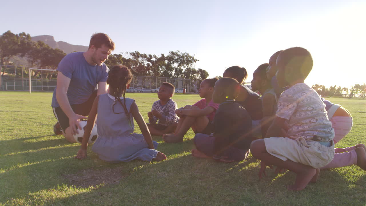 어린 학교 아이 들 과 교사 가 경기장 에서 공 을 가지고 앉아 있다
