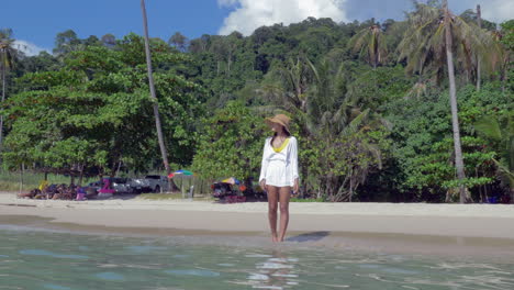 slow motion shot of a woman in a white sundress dipping her toes into the beach