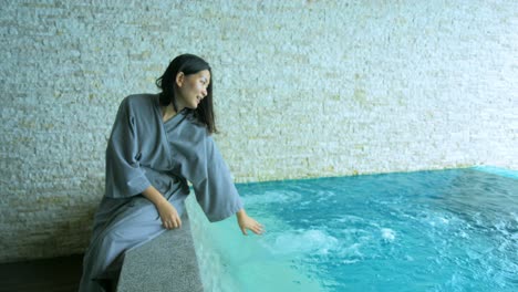 The-soft-and-blur-focus-of-Asia-women-sitting-on-private-poolside-in-the-resort-and-use-her-hand-to-splashing-the-water-on-vacation-time