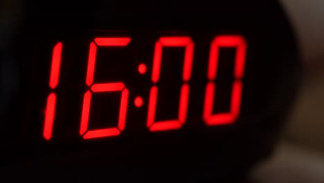 Close-up of black digital clock screen showing 16.00. Blinking red digital numbers on black background. Modern timer system and neon light, electric alarm device