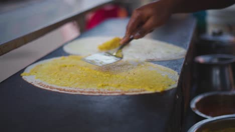 Primer-Plano-De-Dosa-Cocinando-Un-Plato-Del-Sur-De-La-India-Con-Puré-De-Patatas-En-Una-Sartén-De-Hierro-Plano-En-Un-Puesto-De-Comida-Callejera-En-La-India.