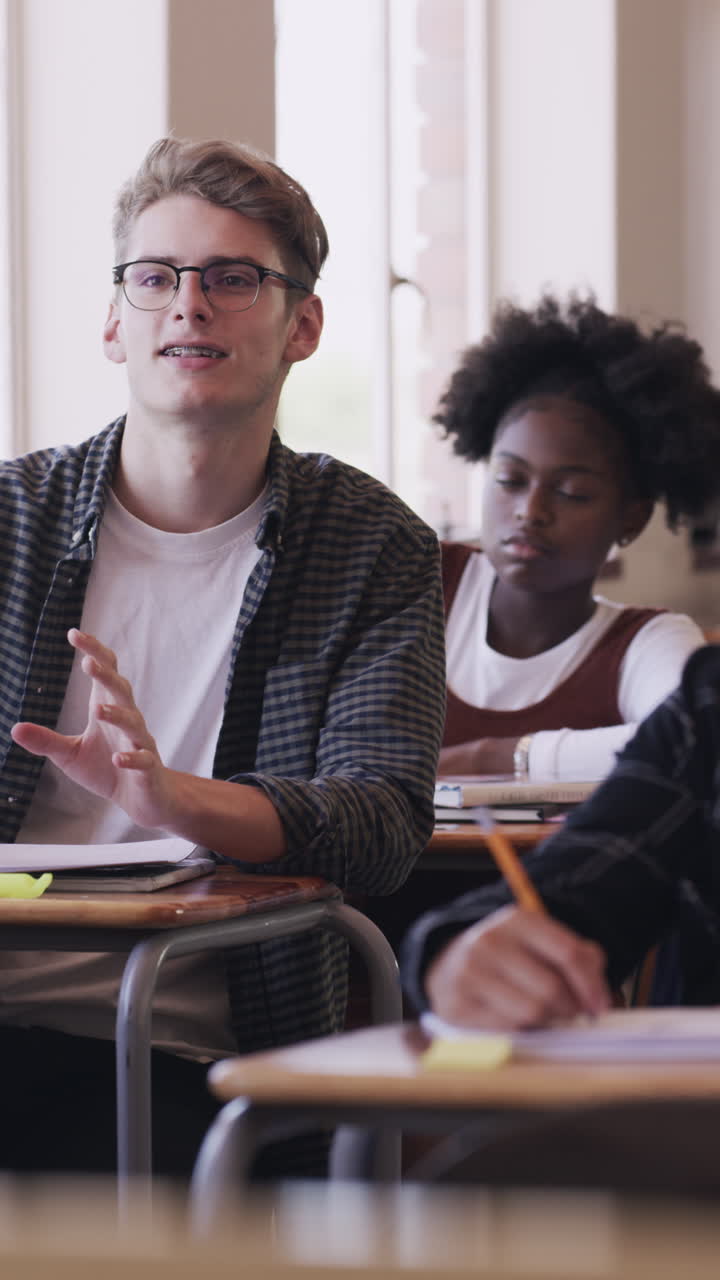 Young Male Student Speaking and Raising Hand in Classroom