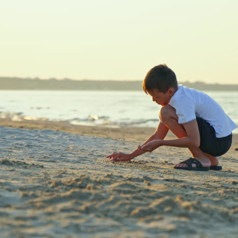 side view of young boy doing something on the sea coast in the evening. summer vacation scene of child playing in the sand beach.