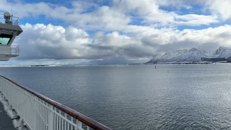 Side-deck-view-on-a-ferry,-showing-a-magnificent-winter-landscape-with-snow-covered-mountains,-panning-shot