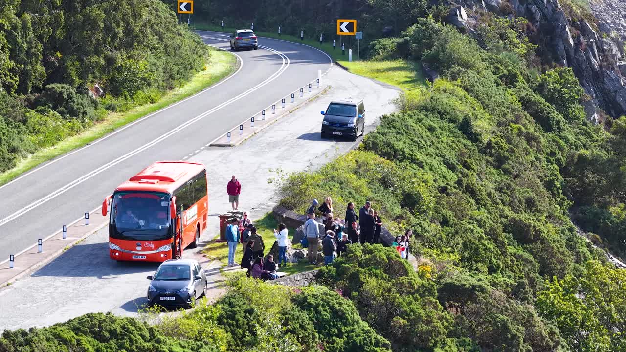 Travelers exit tour bus for roadside stop, bright daylight, lush Scottish landscape, wide aerial view