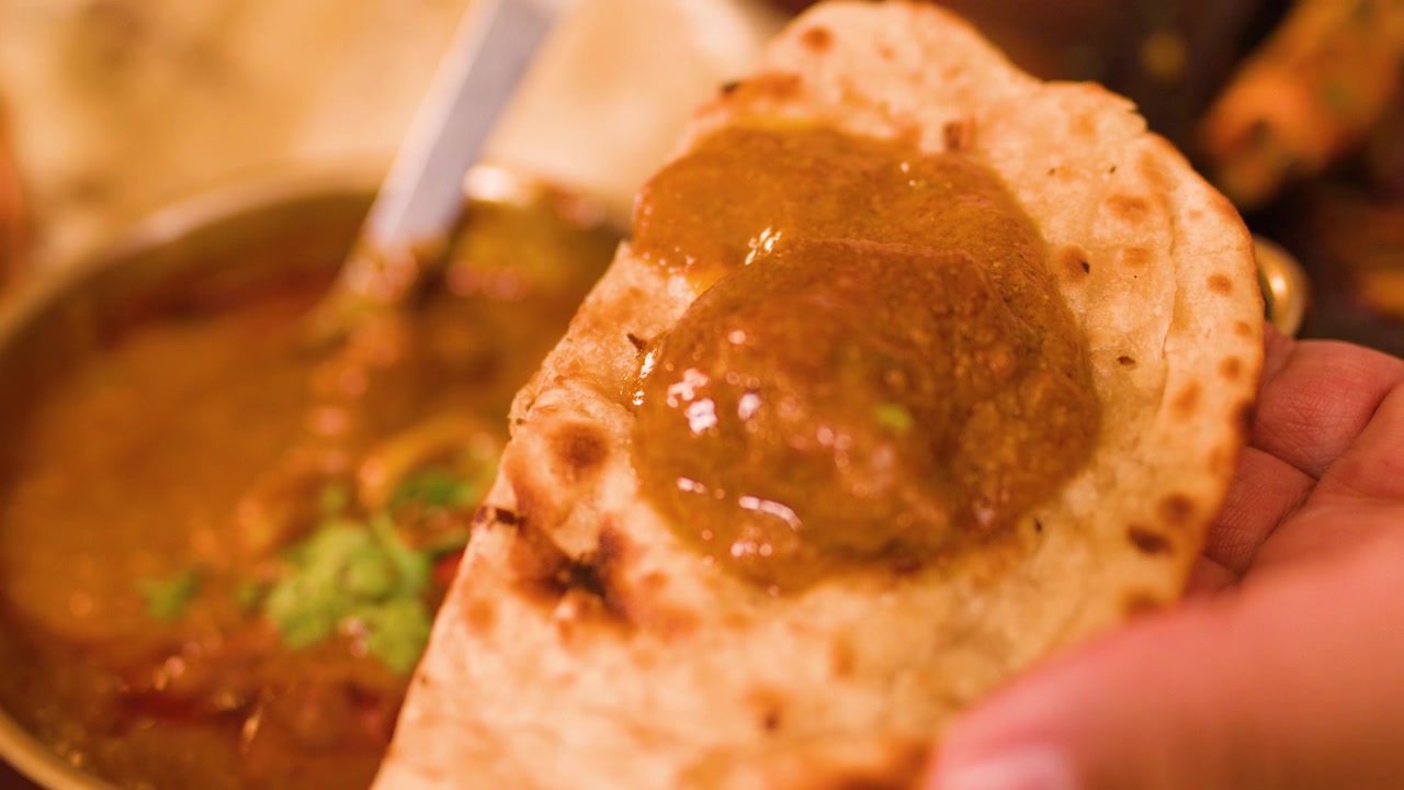 Primo piano di una mano che versa salsa densa sul pane naan, con illuminazione interna calda e suggestiva.