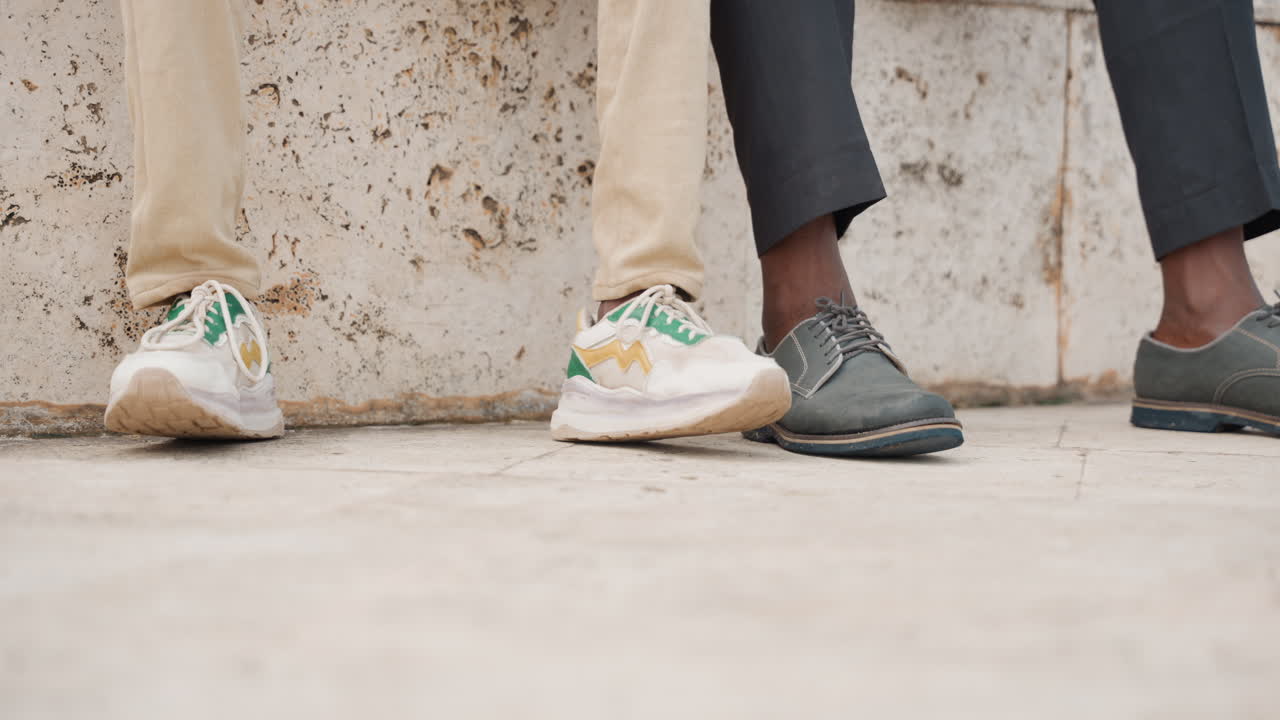 Closeup father and son shoes against concrete wall, casual sneaker and leather shoe, cropped legs and pavement foreground, quiet urban bond, subtle contrast in style, warm afternoon light