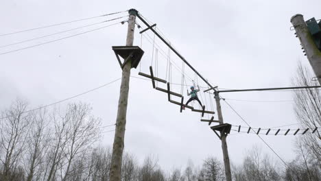 Girl walking across crossed planks on ropes on a high wire adventure obstacle course