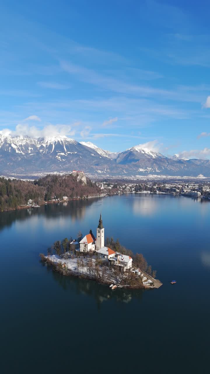 La iglesia en la isla de Bled se encuentra en el tranquilo lago de Bled con los Alpes nevados al fondo, toma vertical cenital con dron