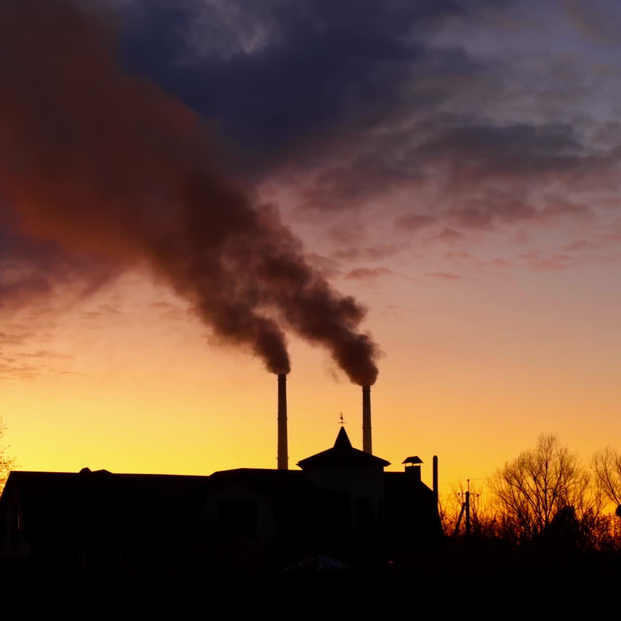 Two pipes rising above the building. Heavy dark smoke gathering in the atmosphere. Sunset landscape